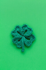 Green crochet shamrock or clover leaf close up on a green background. Happy St. Patrick's day. Top view. Copy space.