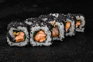 Sushi roll with baked salmon and green onion inside on black concrete background