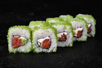 sushi roll with Tuna  inside and green flying fish roe on top on black background