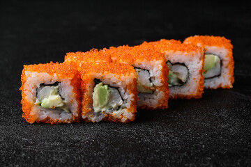 Sushi roll with shrimp inside and red flying fish roe on top on black background