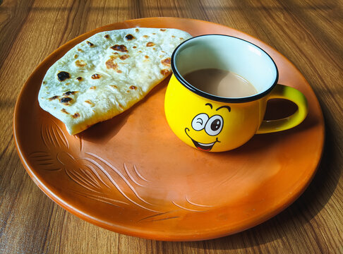 Chai Paratha - Emoji cup Tea served with Flatbread isolated wood background is a traditional simple meal from India, Pakistan and bangladesh