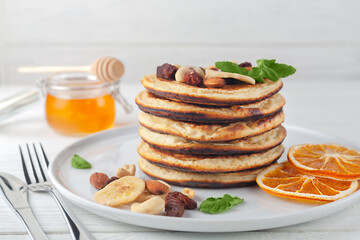 Fresh, delicious pancakes with dried bananas, oranges, nuts and honey on a plate.