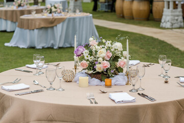 Beautiful outdoor wedding decoration in garden. Round tables decorated with flowers, candles and accessories. Open air wedding banquet on green lawn
