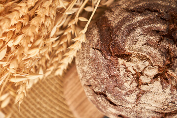 Freshly baked rye bread on a yeast-free starter and on a mixture of whole grain, rye and wheat flour. It lies on a napkin, next to a dried flower with grains. Selective focus. Closeup with copy space.