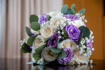 Bridal bouquet made of white and purple roses, eucalyptus leaves lying down on the table. Traditional floral wedding decoration