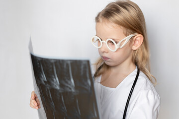 Caucasian child, little doctor, holding and looking at x-ray film, standing on neutral background