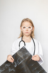 Caucasian child, little doctor, looking sad and serious, holding x-ray film, standing on neutral background