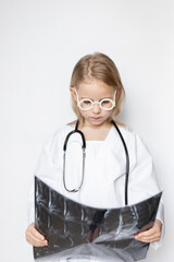 Caucasian child, little doctor, looking thoughtful and serious, holding x-ray film, standing on neutral background