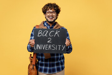 Young happy teen Indian boy IT student he wear casual clothes shirt glasses bag hold card sign with back to university title text isolated on plain yellow color background High school college concept