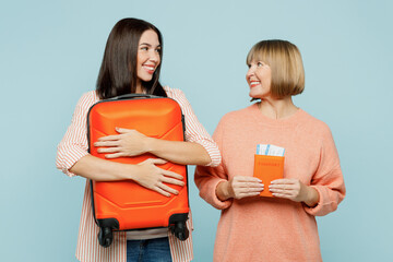 Elder parent mom young adult daughter two women in casual clothes hold passport ticket valise isolated on plain blue background Tourist travel abroad in free time rest getaway Air flight trip concept