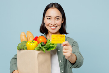 Fototapeta na wymiar Young happy woman in casual clothes hold brown paper bag with food products mock up of credit bank card isolated on plain blue cyan background studio portrait Delivery service from shop or restaurant.