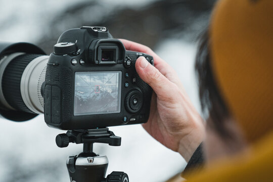 Close up view of male photographer using the rear lcd screen to compose and take a landscape photo with his digital camera dsrl using liveview. Outdoor snowy swiss mountains