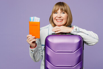 Traveler elderly woman 50s years old in casual clothes hold suitcase passport ticket isolated on plain purple background Tourist travel abroad in free spare time rest getaway Air flight trip concept