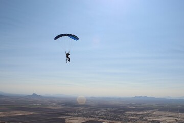Skydive flys parachute over Arizona on a beautiful sunny afternoon with mountains in the background.