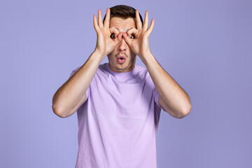 Young handsome man doing gesture like binoculars