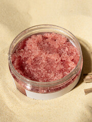 Pink body scrub in plastic jar. Sugar scrub with strawberries for body, face. Home care. Jar on sand