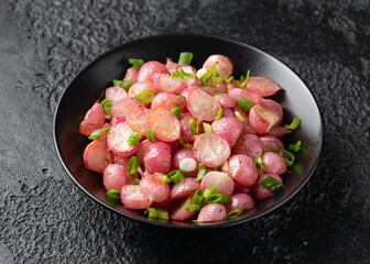 Roasted radish with spring onion and herbs in a black bowl