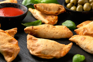 Freshly baked mini calzones with bolognese served on black slate board