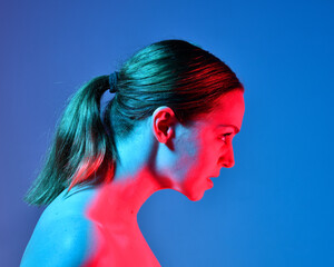 Naklejka premium Head and shoulders close up portrait of pretty girl with expressive facial expressions, with colourful neon gel lighting, isolated on studio background.