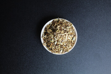 Dried granules of Aniseed, or Pimpinella Anisum seed, or Adas Manis, inside a bowl. Isolated on black background. Flat lay or top view