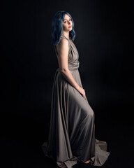 Fototapeta premium close up portrait of pretty girl with blue hair wig & elegant gown with expressive facial expressions & gestural arm poses. colourful neon gel lighting, isolated on studio background.