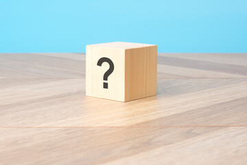 cube with question mark on wooden background, closeup