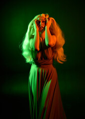 portrait of pretty girl with blonde hair & elegant gown with expressive facial expressions & gestural arm poses. colourful neon gel lighting, isolated on black studio background.