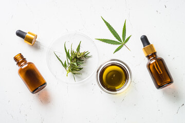 CBD oil and cannabis leaves at white table. Medicine and cosmetic product. Flat lay image.