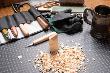 Carving tools on a cutting mat with basswood, shavings, gloves, knives, and coffee mug