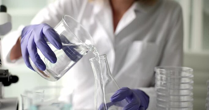 Scientist chemist pours water from transparent bottle into a flask in laboratory
