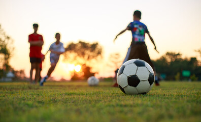 action sport outdoors of a group of kids having fun playing soccer football for exercise and recreation at the green grass field in community rural area under the twilight sunset sky