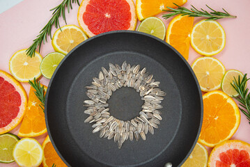 background of slices of citrus fruits, oranges, lemons, limes, grapefruits, on which a black pan is placed, inside which a sunflower flower is made from sunflower seeds. View from the top.