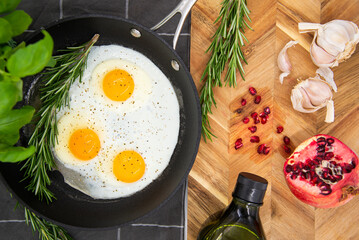 breakfast or brunch, fried eggs in black pans and red pomegranate with garlic and basil. view from the top.