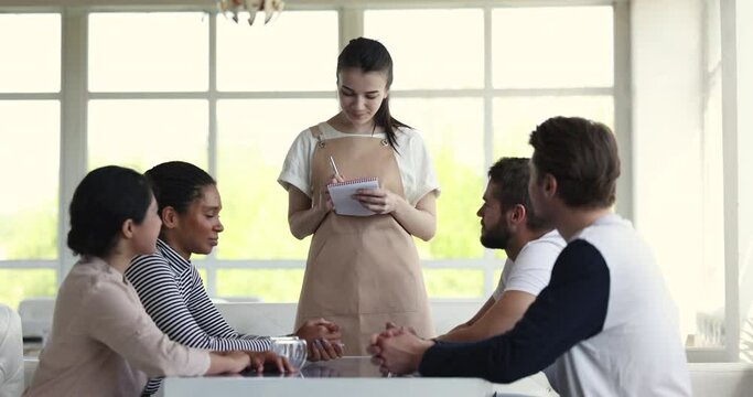 Diverse friends, restaurant guests, make order talk to waitress in apron hold notepad take notes. Female waiter serving cafe clients, smile looks polite, provide professional services, doing job well