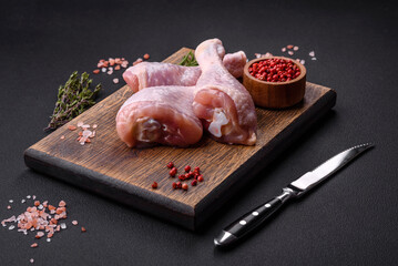 Three raw chicken legs with spices and herbs on a wooden cutting board