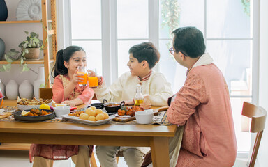 Portrait of happy Indian family, father, son, daughter wearing traditional clothes, sitting at table together for breakfast, lunch or dinner, eating and fun talking with warm. Lifestyle Concept.