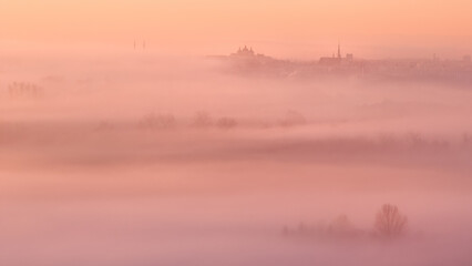 Panorama of the city: Towers and Temples rising out of the ground fog of the agricultural landscape. Pastel colours of sunrise, warm tones, ground fog, frosty morning. No snow  Winter.