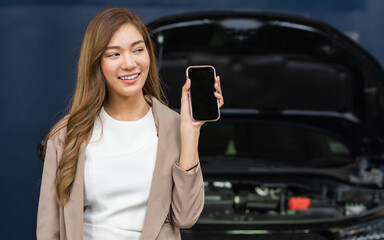 Portrait adult beautiful Asian female customer smiling, satisfied, positive evaluation with car maintenance service, showing, holding, using mobile phone for payment. Service, Industry Concept.
