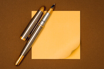 A fountain pen and blank yellow sticky note waiting for your message