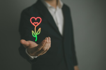 Man handing heart shape on hand a red heart There are green flower stalks.