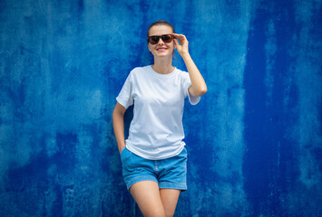 Female model wearing white blank t-shirt on the background of an blue wall.