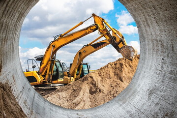 Two powerful excavators work at the same time on a construction site, sunny blue sky in the...