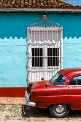 Red vintage car parked in front of a blue colonial house in the old center of Trinidad, Cuba, Caribbean