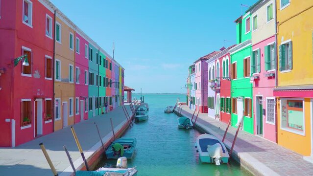 Bright multi-colored semi-detached houses stand along lagoon water channel banks at bright sunlight under clear blue sky in Burano