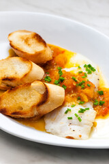 white fish with tomato sauce and roasted baguette slices