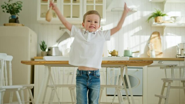 Playful small child boy is dancing, playing and singing jumping in kitchen.