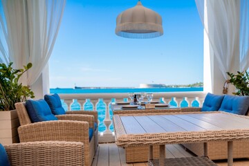 Cafe sea no one. Empty street cafe with wicker furniture on the beach. Overlooking the sea on a sunny summer day, coastline on the horizon and blue sky.
