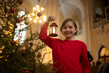 the boy holds a red flashlight, stands near the Christmas tree in the Catholic Church, after the...