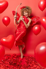 Arrow of love. Positive smiling woman being cupid angel poses with bow shoots in someone stands in full length against bright red background helps people to find love. St Valentines Day concept