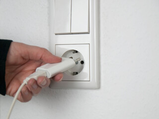 Energiekosten und Stromverbrauch: Hand beim Einstecken eines weißen Steckers in die weiße...